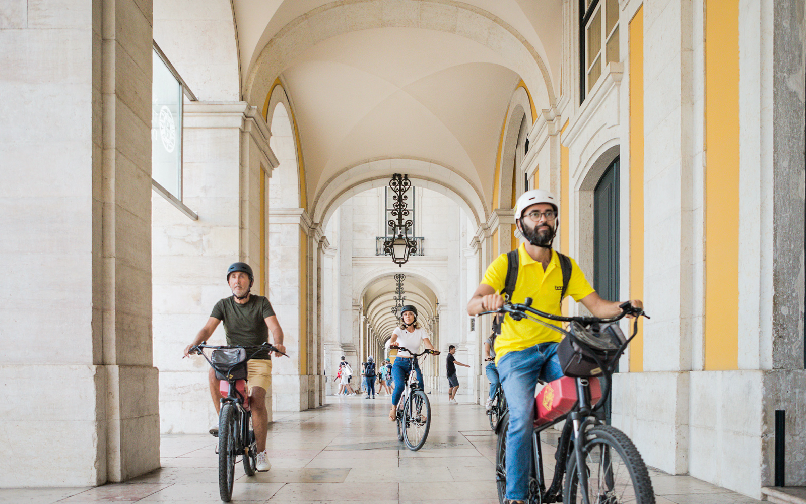 Cyclists riding e-bikes through an arched corridor in Lisbon, Portugal.