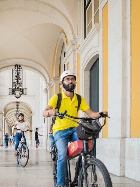 Cyclists riding e-bikes through an arched corridor in Lisbon, Portugal.