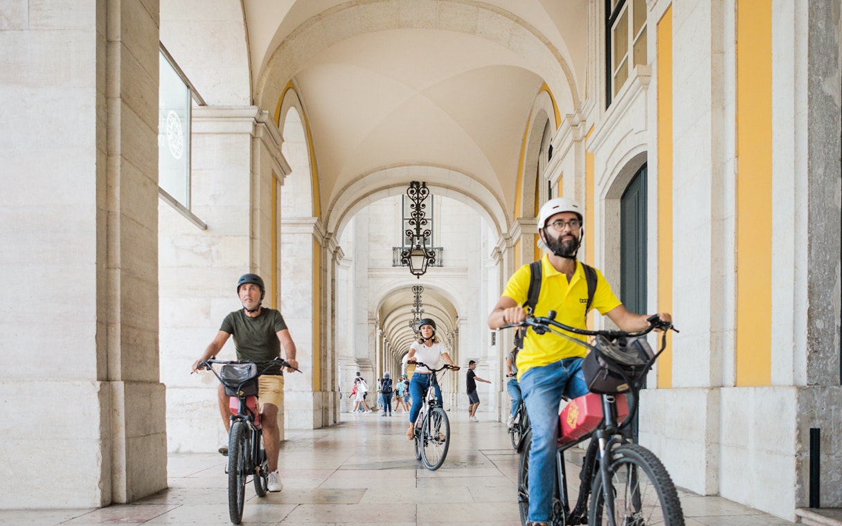 Cyclists riding e-bikes through an arched corridor in Lisbon, Portugal.