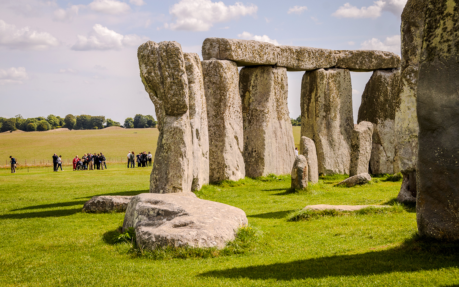 Stonehenge with tourists in the background, grassy field, clear sky, near London.