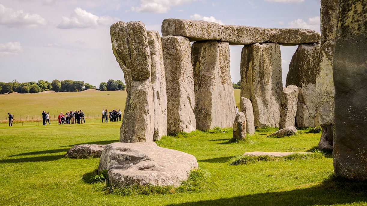 Stonehenge with tourists in the background, grassy field, clear sky, near London.