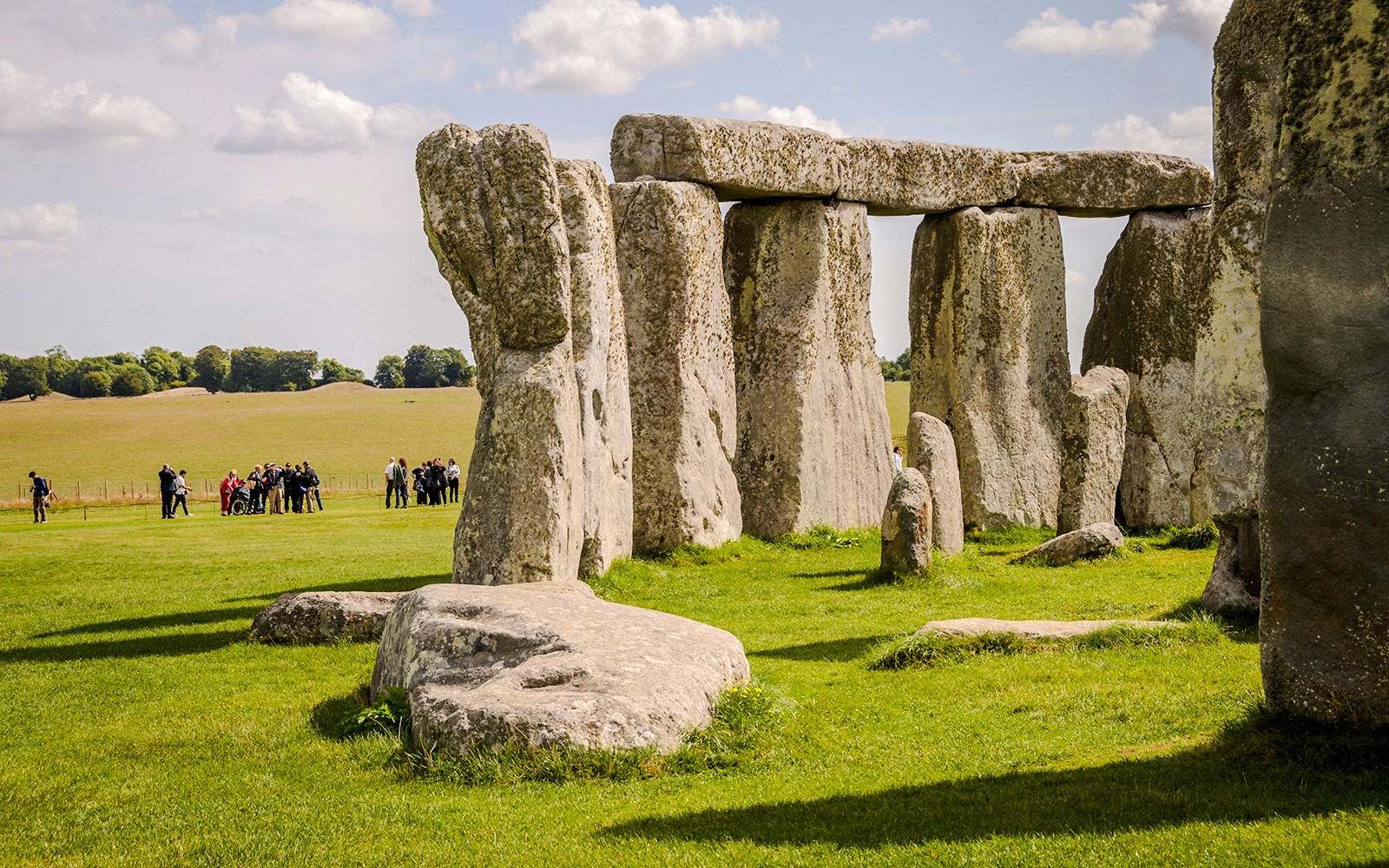 Stonehenge with tourists in the background, grassy field, clear sky, near London.