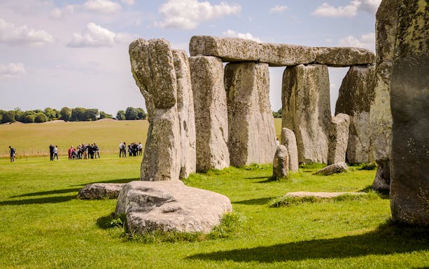 Stonehenge with tourists in the background, grassy field, clear sky, near London.