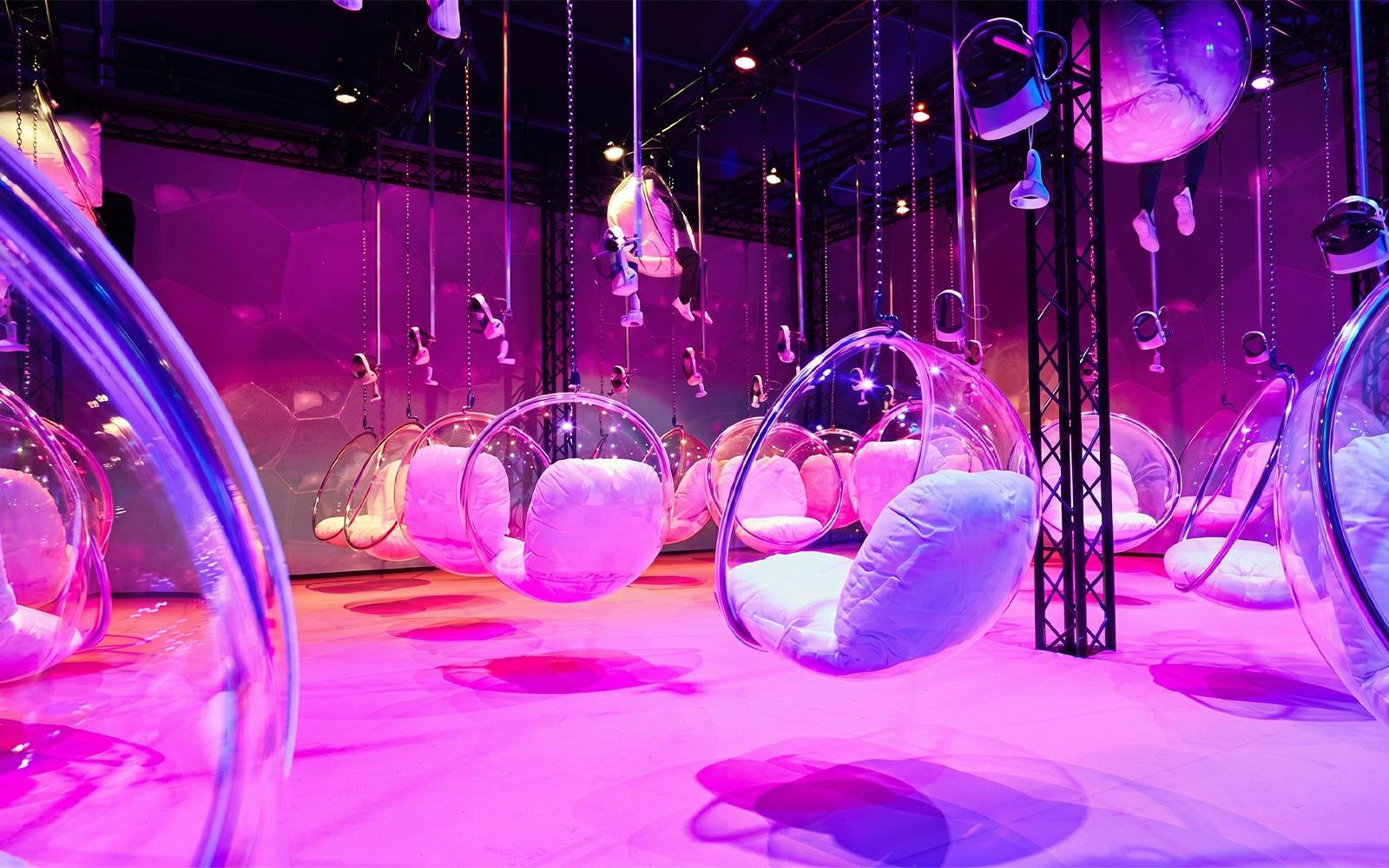 Hanging bubble chairs with cushions in a vibrant pink-lit room at Bubble Planet, Phoenix, Arizona.