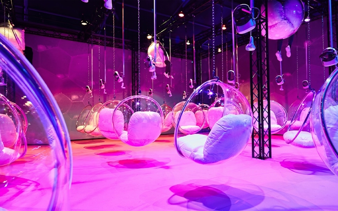 Hanging bubble chairs with cushions in a vibrant pink-lit room at Bubble Planet, Phoenix, Arizona.
