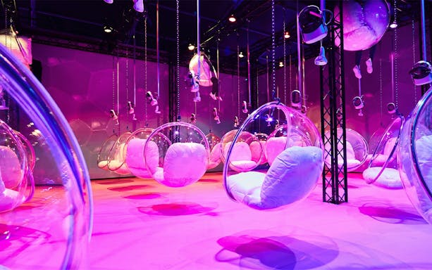 Hanging bubble chairs with cushions in a vibrant pink-lit room at Bubble Planet, Phoenix, Arizona.
