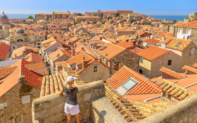 Aerial view of Dubrovnik's red rooftops with a girl on the city walls, Croatia.