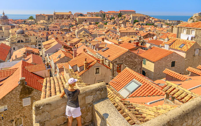 Aerial view of Dubrovnik's red rooftops with a girl on the city walls, Croatia.