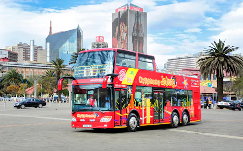 Hop-On Hop-Off red bus in Johannesburg city center with skyline in background.