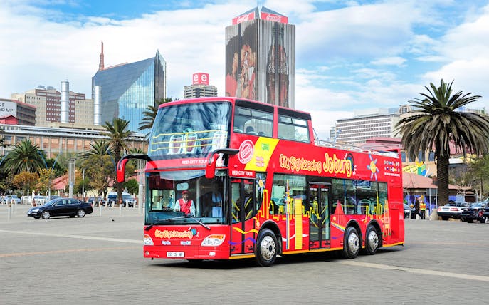 Hop-On Hop-Off red bus in Johannesburg city center with skyline in background.