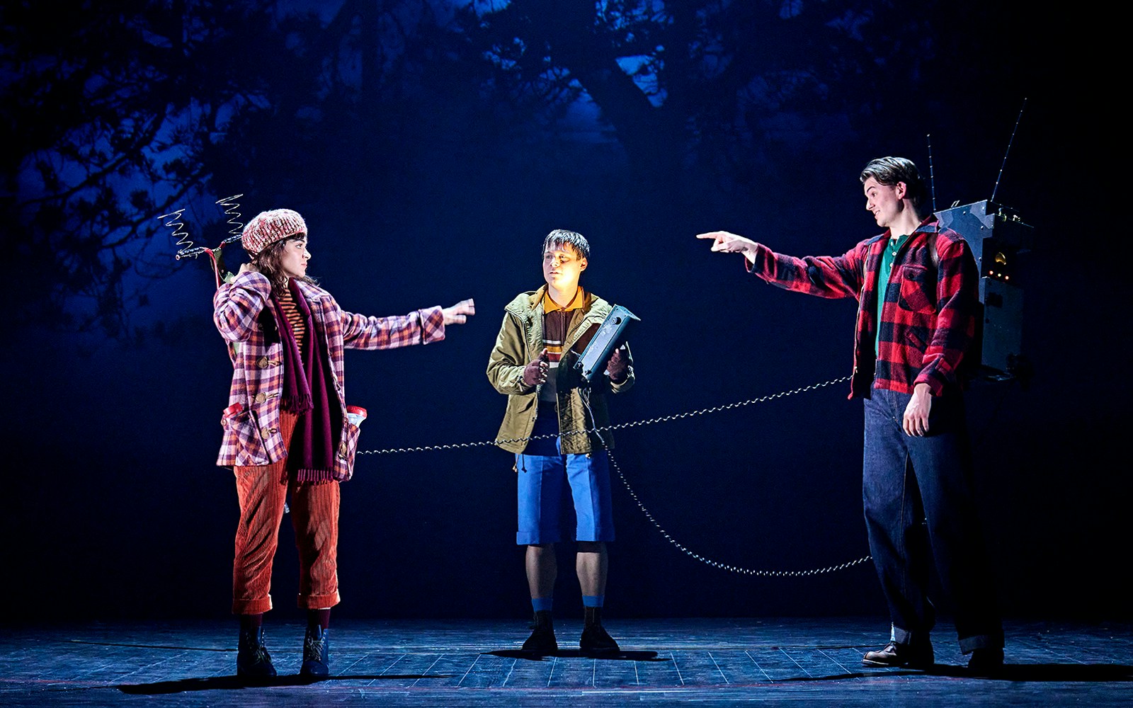 Three actors on stage in a scene from "Stranger Things: The First Shadow," with one holding a device.