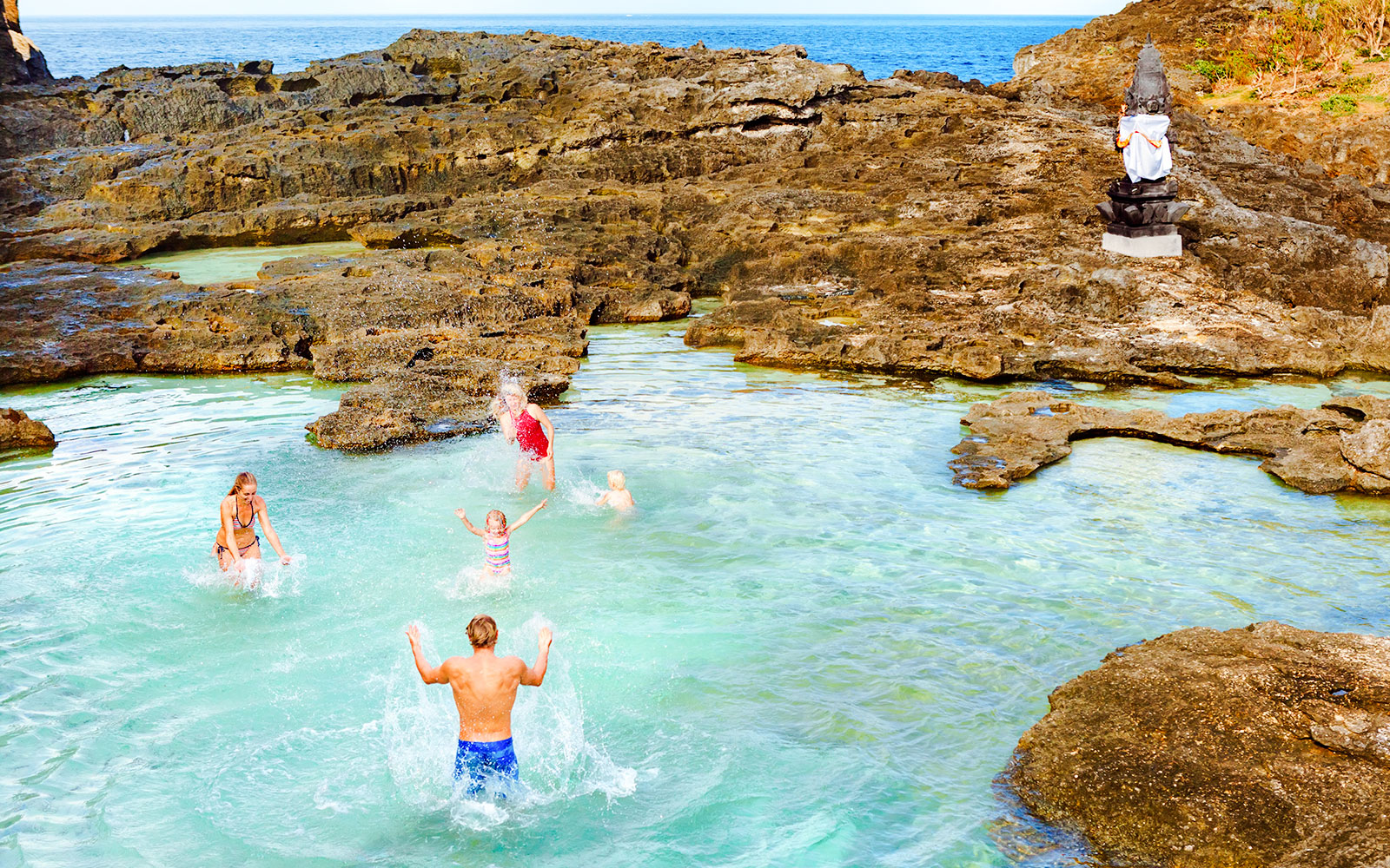People enjoying Angel’s Billabong natural pool with rocky cliffs in Nusa Penida, Indonesia.