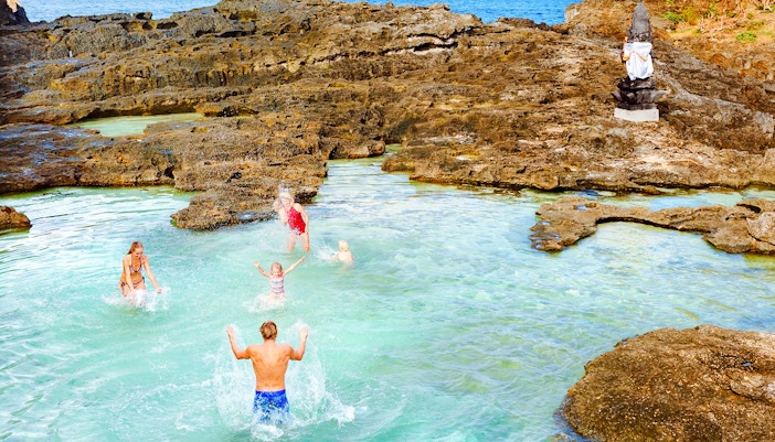 People enjoying Angel’s Billabong natural pool with rocky cliffs in Nusa Penida, Indonesia.