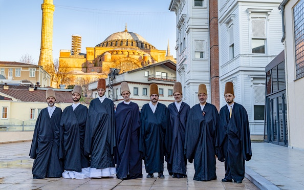 Whirling dervishes in traditional attire standing in front of Hagia Sophia, Istanbul.