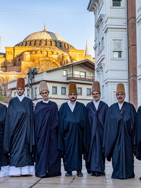 Whirling dervishes in traditional attire standing in front of Hagia Sophia, Istanbul.