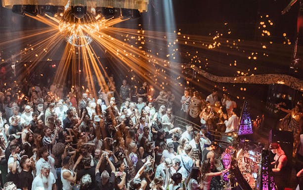 DJ performing at Club Chinois with a lively crowd under a disco ball.