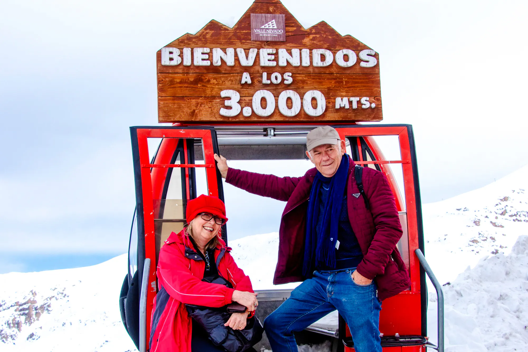 Couple at Valle Nevado ski lift, Santiago, with snowy mountains in the background.
