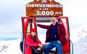 Couple at Valle Nevado ski lift, Santiago, with snowy mountains in the background.