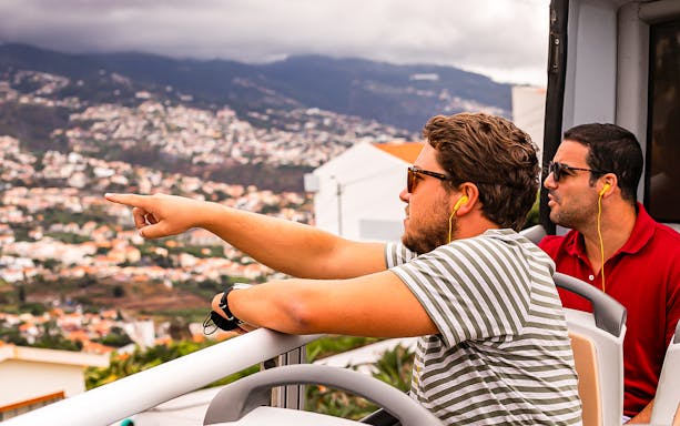 Tourists on Madeira hop-on hop-off bus enjoying city view.