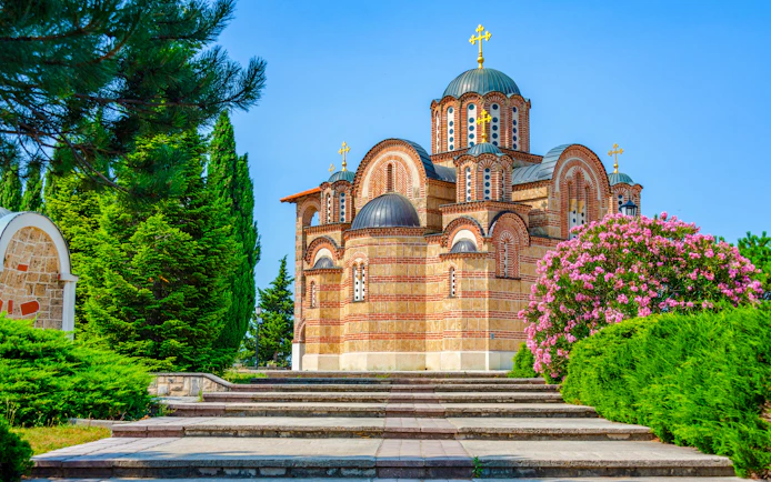 Hercegovacka Gracanica Temple with domes and arches in Trebinje, Bosnia, surrounded by greenery.
