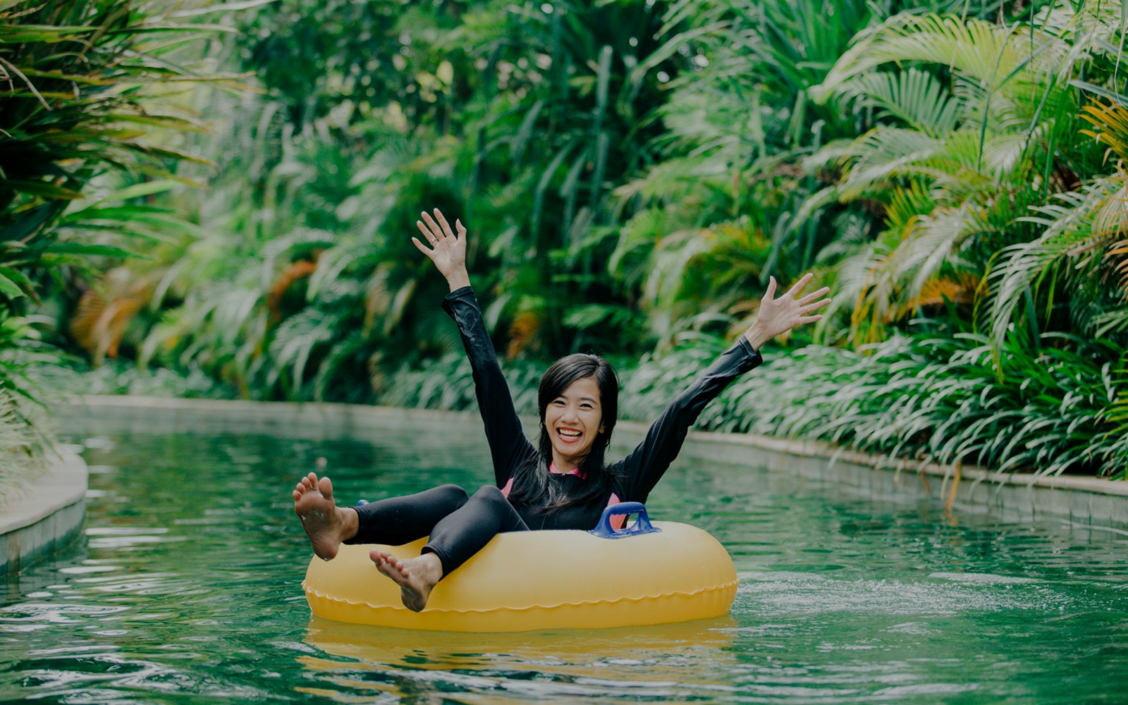 Young woman tubing in a lush, tropical lazy river.