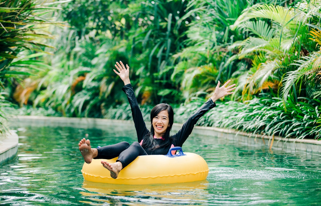 Young woman tubing down a lazy river surrounded by lush greenery in a tropical setting.