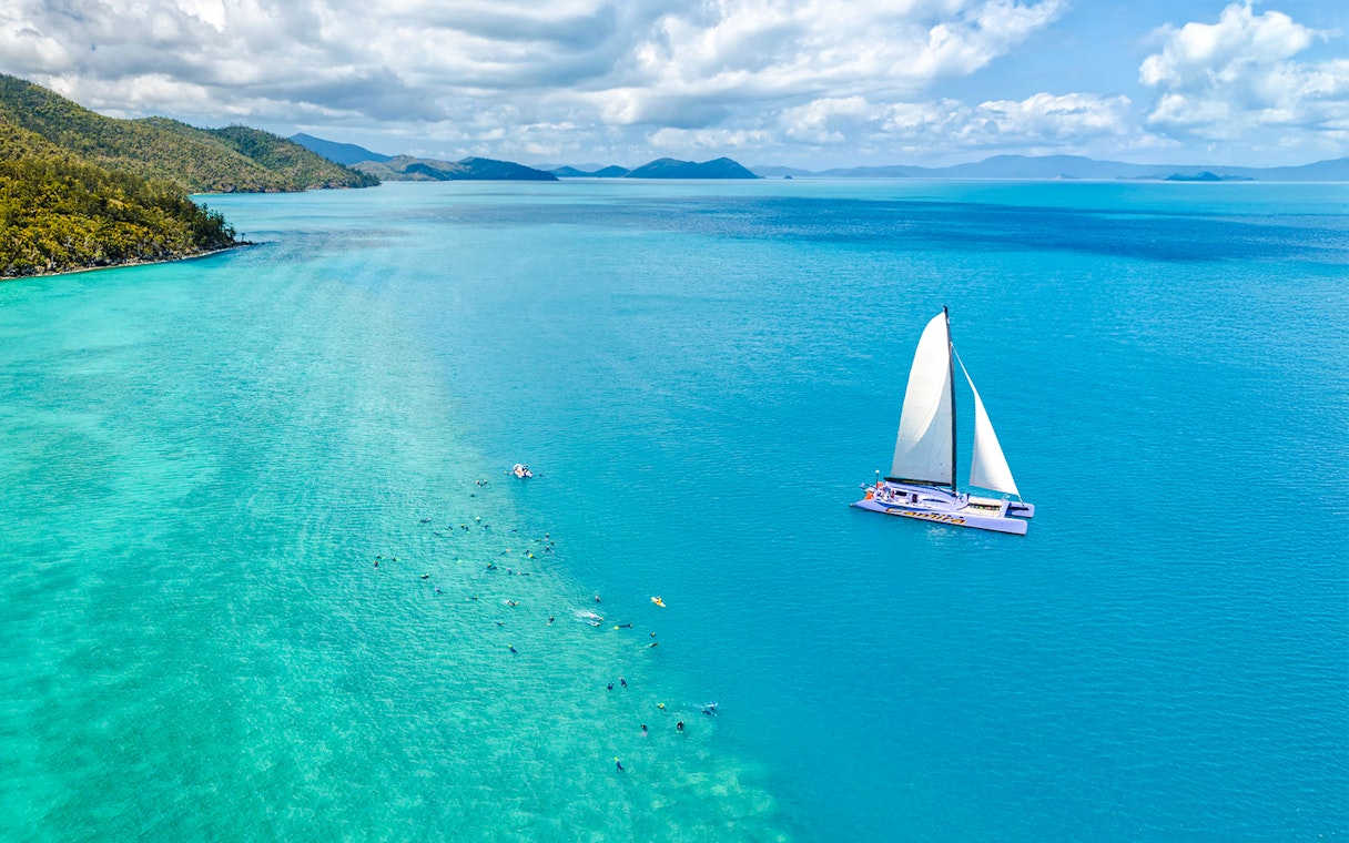 Sailing catamaran on turquoise waters near Airlie Beach with snorkelers in the ocean.