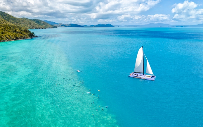 Sailing catamaran on turquoise waters near Airlie Beach with snorkelers in the ocean.