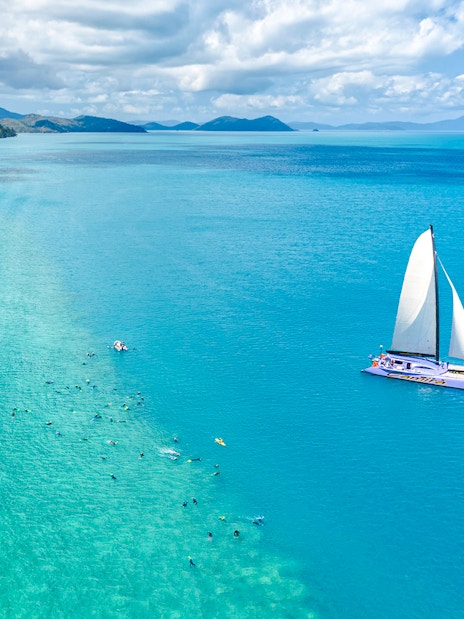 Sailing catamaran on turquoise waters near Airlie Beach with snorkelers in the ocean.