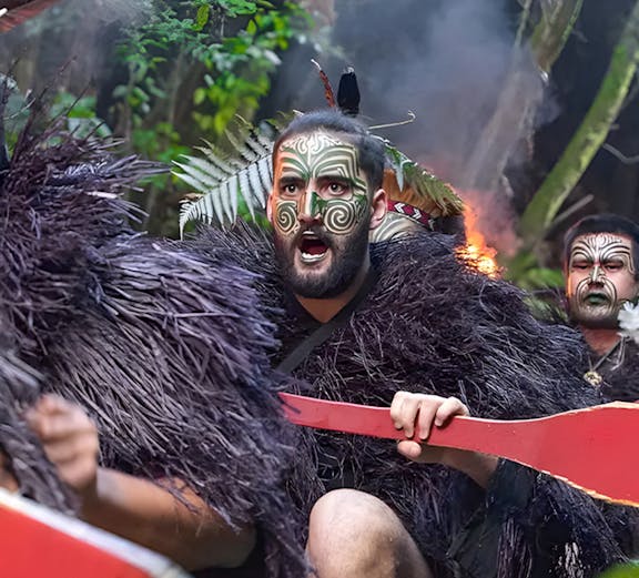 Warriors paddling a canoe at Mitai Maori Village, New Zealand.