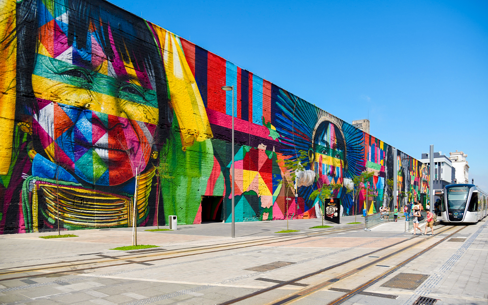 Tourists walking along Olympic Boulevard beside vibrant mural in Rio de Janeiro.