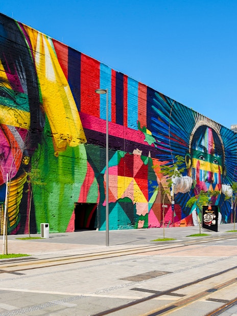 Tourists walking along Olympic Boulevard beside vibrant mural in Rio de Janeiro.