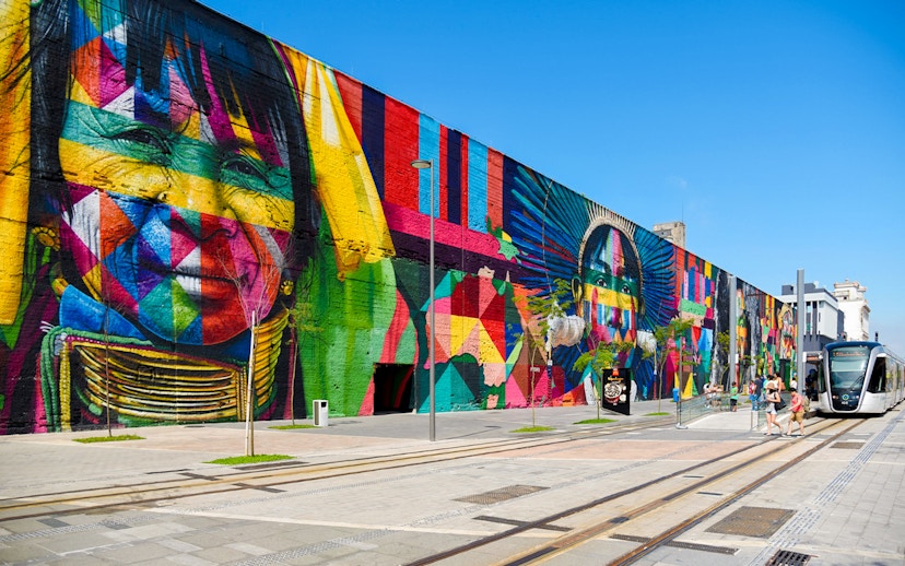 Tourists walking along Olympic Boulevard beside vibrant mural in Rio de Janeiro.