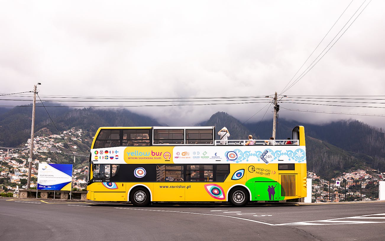 Open-top yellow tour bus on Madeira's scenic route with mountains in the background.