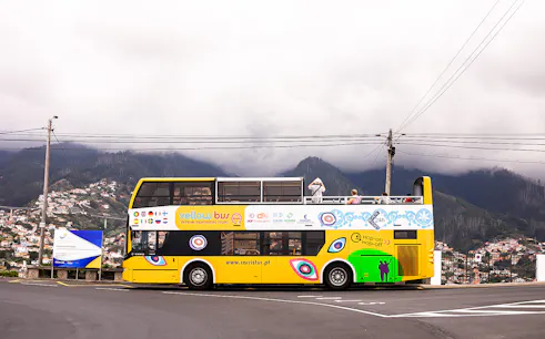 Open-top yellow tour bus on Madeira's scenic route with mountains in the background.