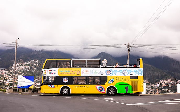 Open-top yellow tour bus on Madeira's scenic route with mountains in the background.