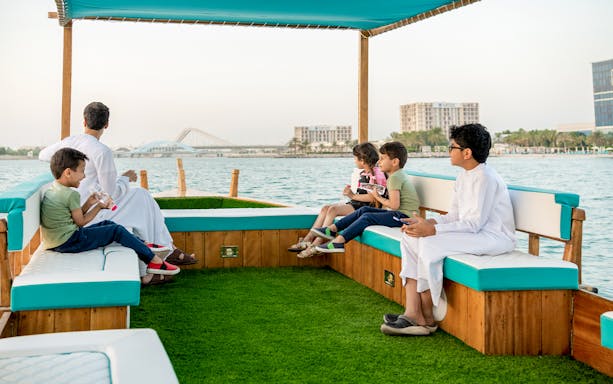 Family enjoying a boat cruise with cityscape view in Abu Dhabi.