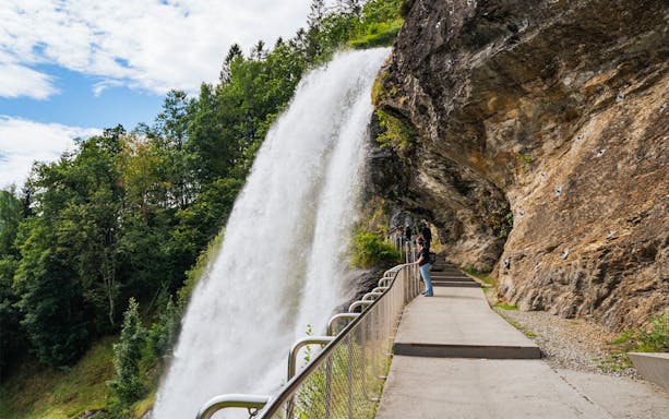 Tourists walking behind Steinsdalsfossen waterfall in Norway.