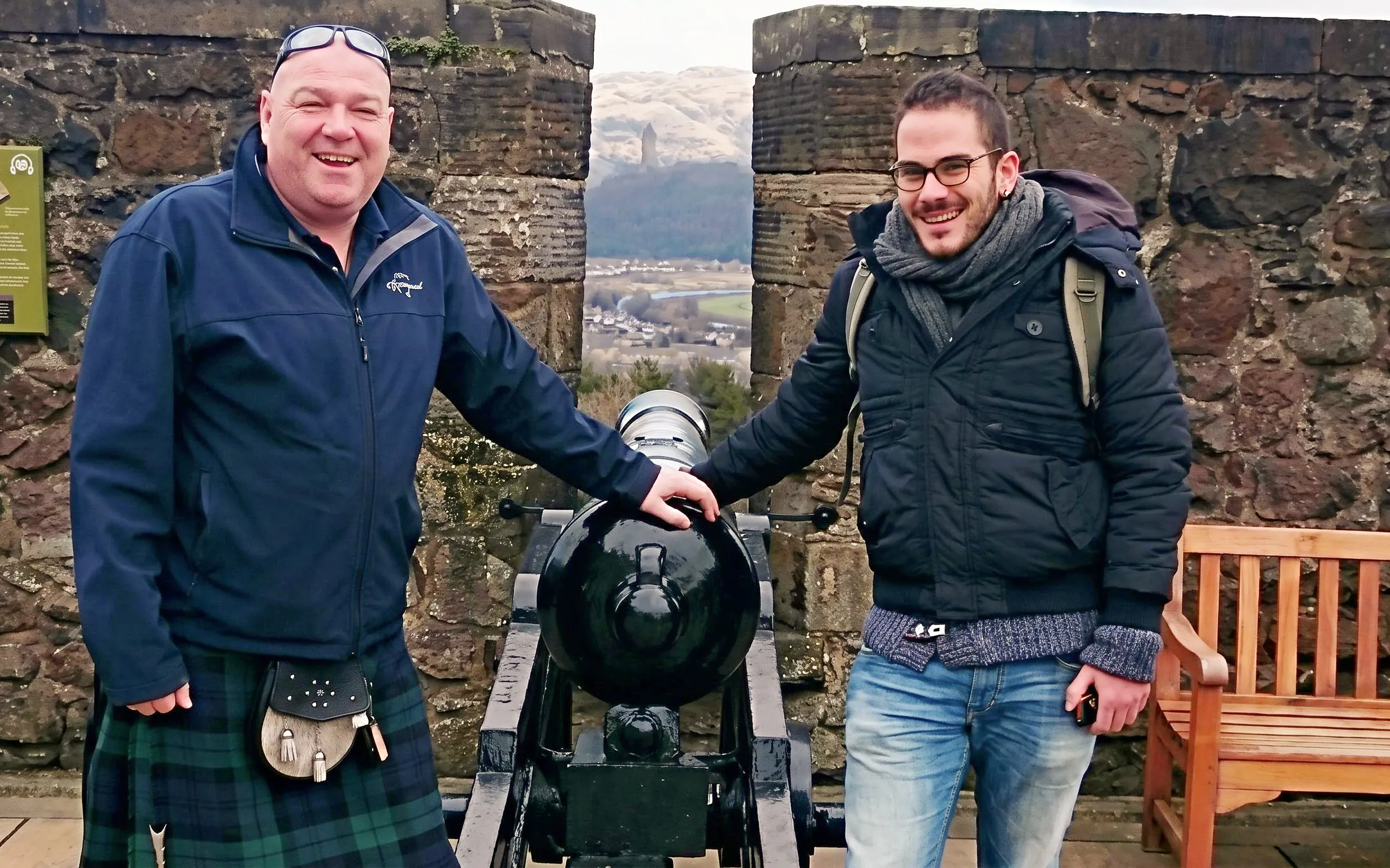 Two visitors standing by a cannon at Stirling Castle with a scenic view in the background.
