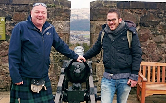 Two visitors standing by a cannon at Stirling Castle with a scenic view in the background.