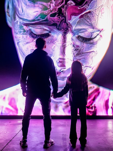 Visitors at AMAZE Amsterdam viewing a large, colorful digital face display.