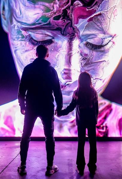 Visitors at AMAZE Amsterdam viewing a large, colorful digital face display.
