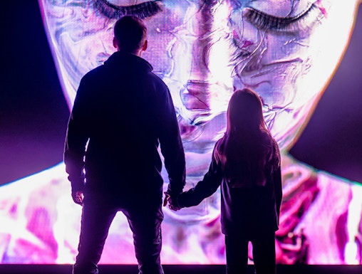 Visitors at AMAZE Amsterdam viewing a large, colorful digital face display.