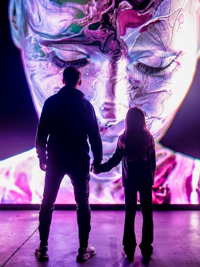 Visitors at AMAZE Amsterdam viewing a large, colorful digital face display.