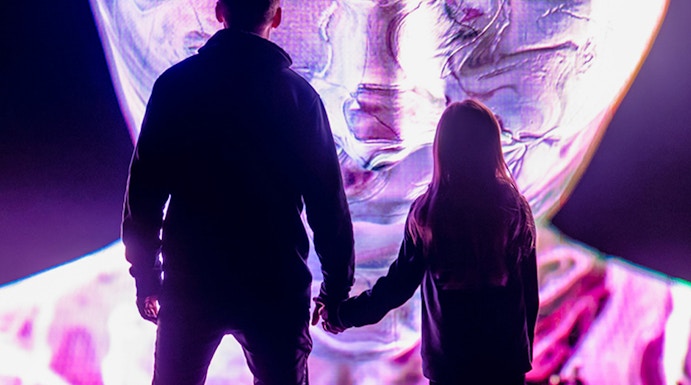 Visitors at AMAZE Amsterdam viewing a large, colorful digital face display.