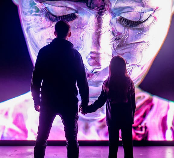 Visitors at AMAZE Amsterdam viewing a large, colorful digital face display.