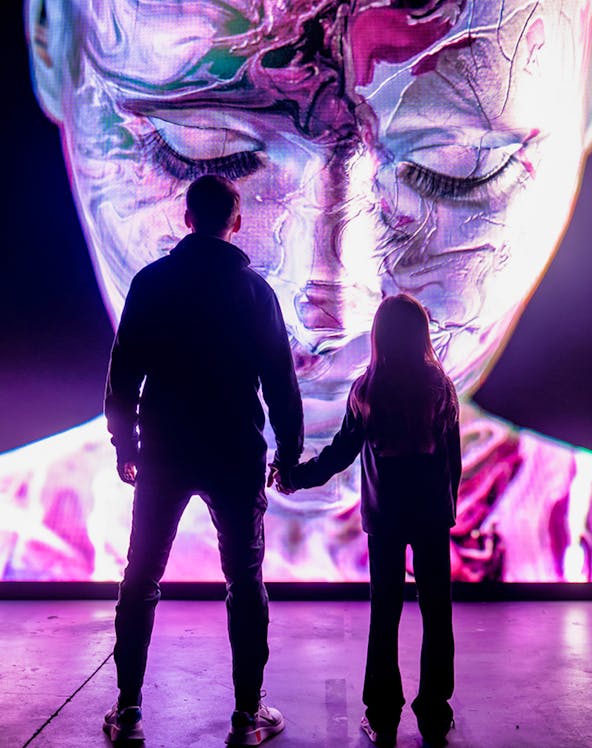 Visitors at AMAZE Amsterdam viewing a large, colorful digital face display.