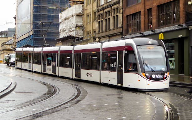 Edinburgh tram on city street for airport transfer.