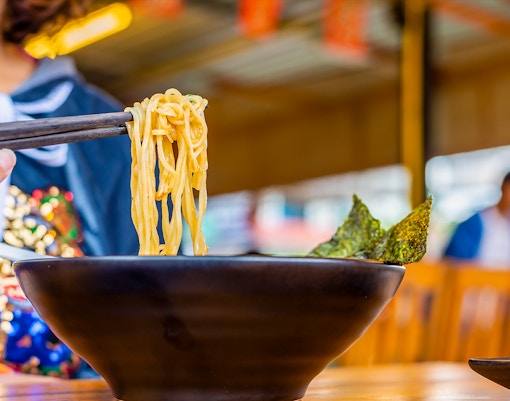 Chopsticks lifting ramen noodles from a bowl during a cooking experience.