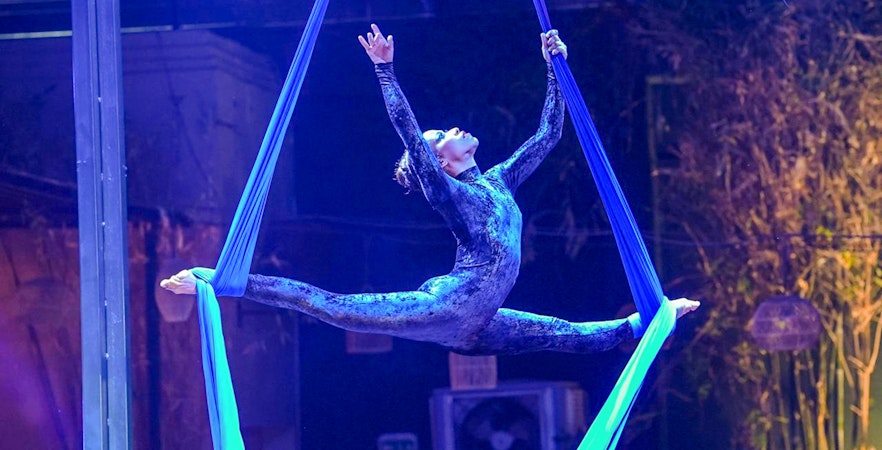 Aerial performer at Nouba Restaurant Dinner Show in a split pose on blue silks.
